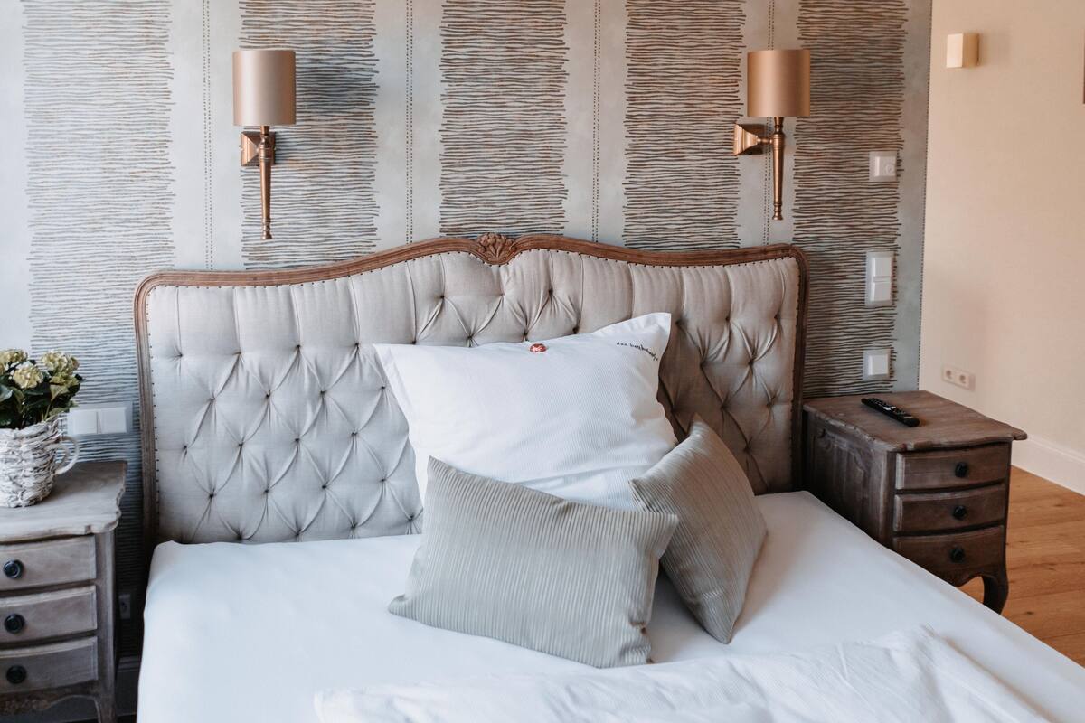 Een slaapkamer met een gestoffeerd hoofdeinde, een nachtkastje met een lamp en een nachttafel met een afstandsbediening.