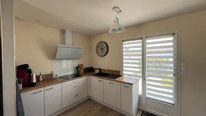 A modern kitchen with white cabinets, a wooden countertop, a built-in oven, and a window with blinds. - Comfortable vacation home ideally located between beach and town center (Saint-Hilaire-de-Riez)