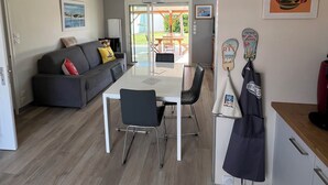 A modern living space with a dining area, a sofa, a kitchen, and a view through a glass door to an outdoor patio. - Comfortable vacation home ideally located between beach and town center (Saint-Hilaire-de-Riez)