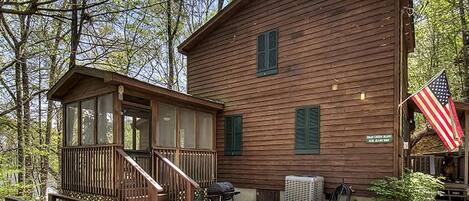 A wooden cabin with a porch, a grill, and an American flag.