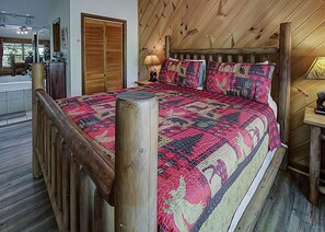 Een slaapkamer met een houten hoofdbord, een groot bed met een bedovertrek met patroon, een nachtkastje met een lamp en een houten garderobe.