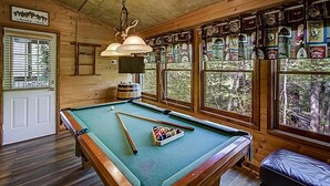 Une table de billard dans une pièce aux murs en bois et aux grandes fenêtres.