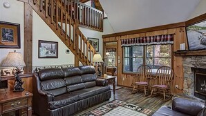 Un salon chaleureux avec un canapé en cuir, un plancher en bois, une cheminée et un escalier.