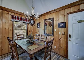 Een eetzaal met een houten tafel, stoelen, een kroonluchter en een deur met een bordje.