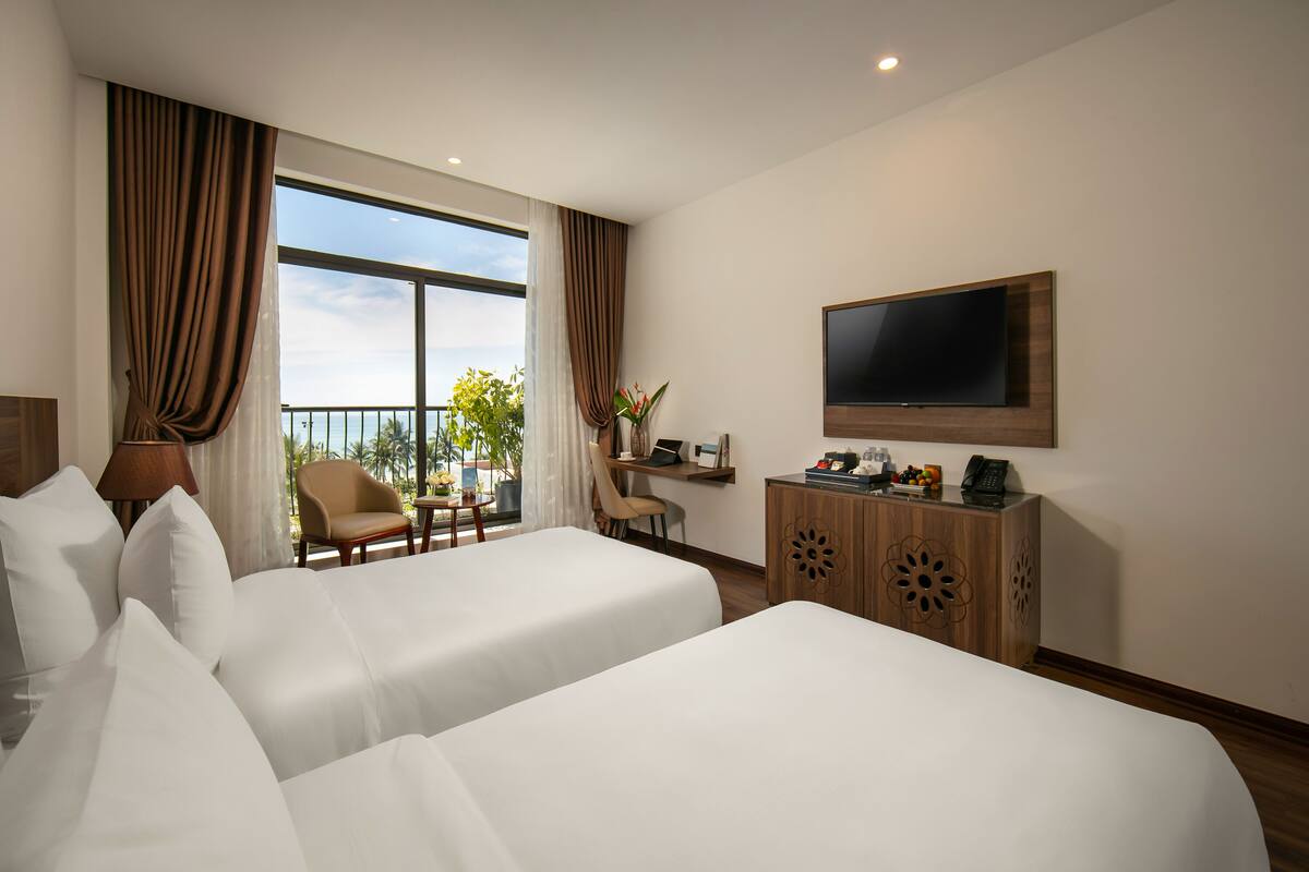 Ein Hotelzimmer mit zwei Betten, einem Schreibtisch, einem Sessel, einem Fernseher und Blick ins Freie.