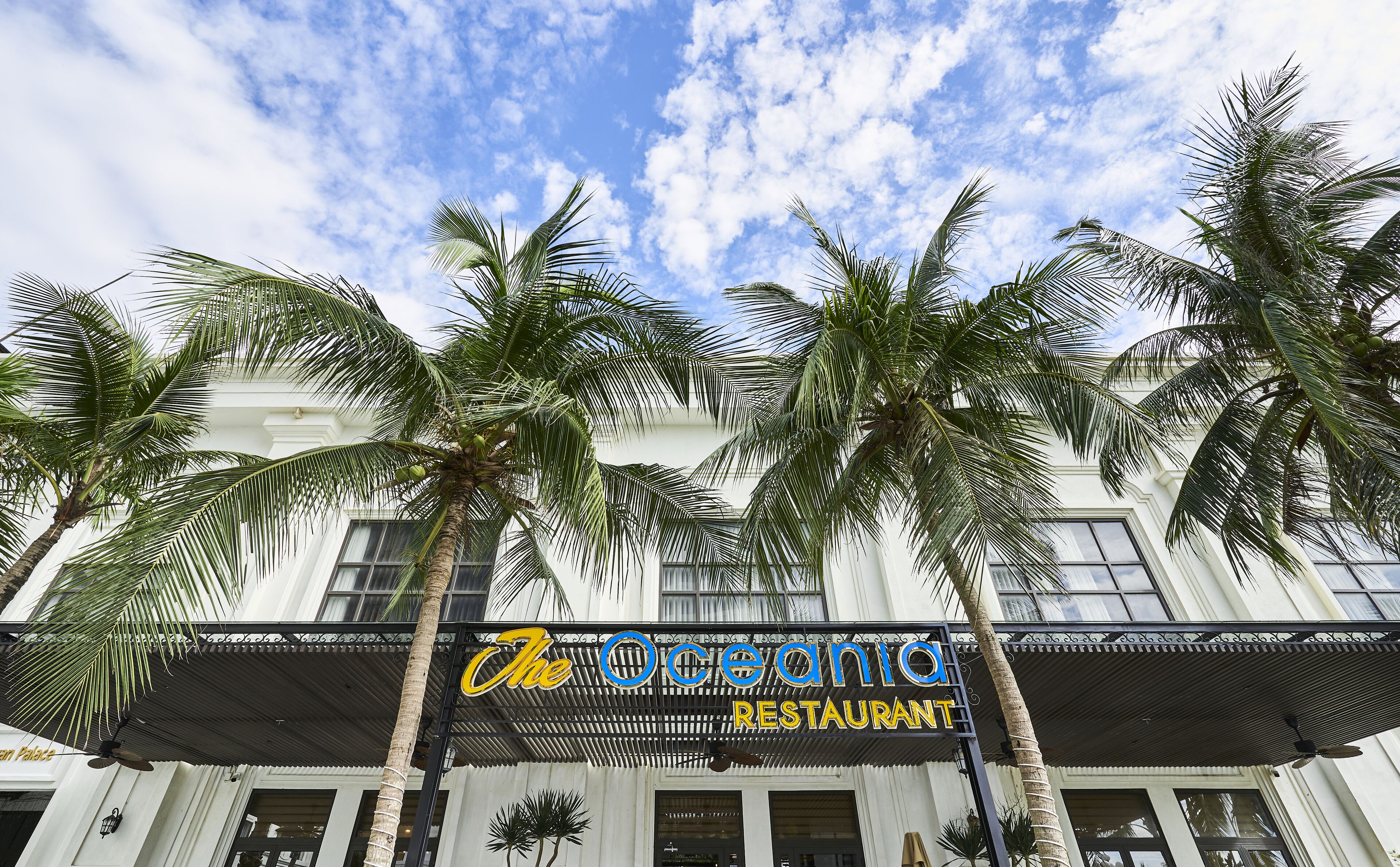 The Oceania Restaurant with a white facade, palm trees, and a clear blue sky.