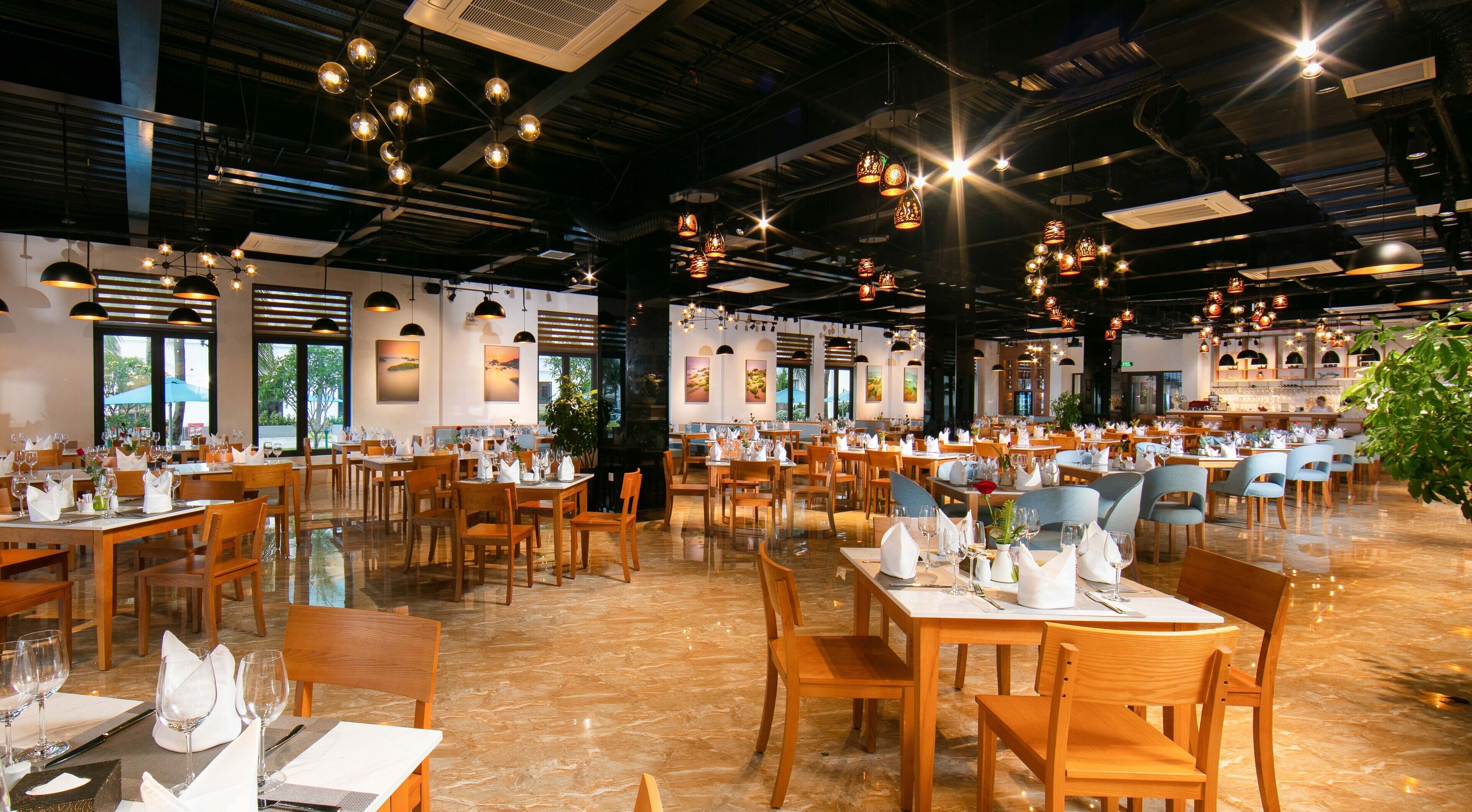 A spacious restaurant with multiple dining areas, wooden tables and chairs, and hanging pendant lights.