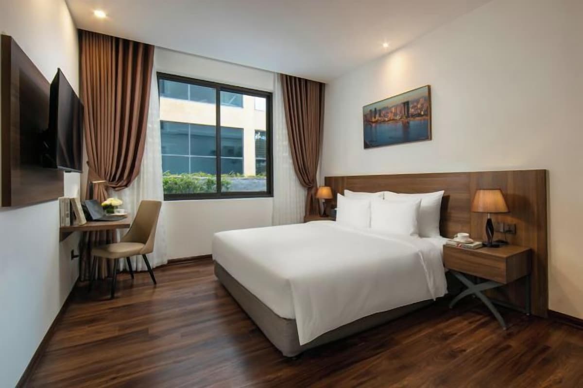 A hotel room with a large bed, a desk with a chair, a TV, and a painting on the wall.