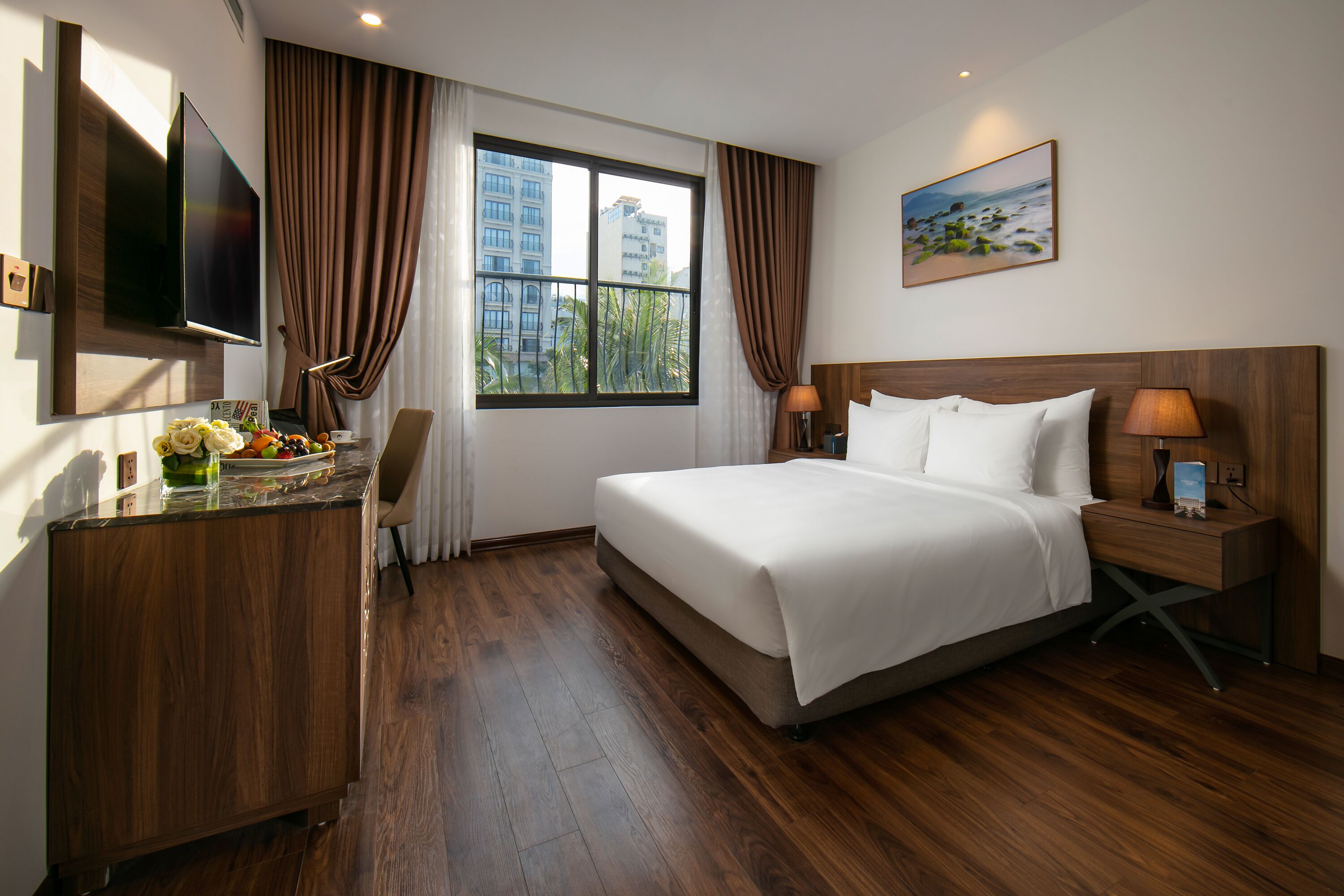 A hotel room with a large bed, a desk with a flat-screen TV, a lamp, and a window with curtains.