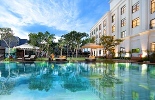 A pool area with lounge chairs, umbrellas, and a building with balconies.