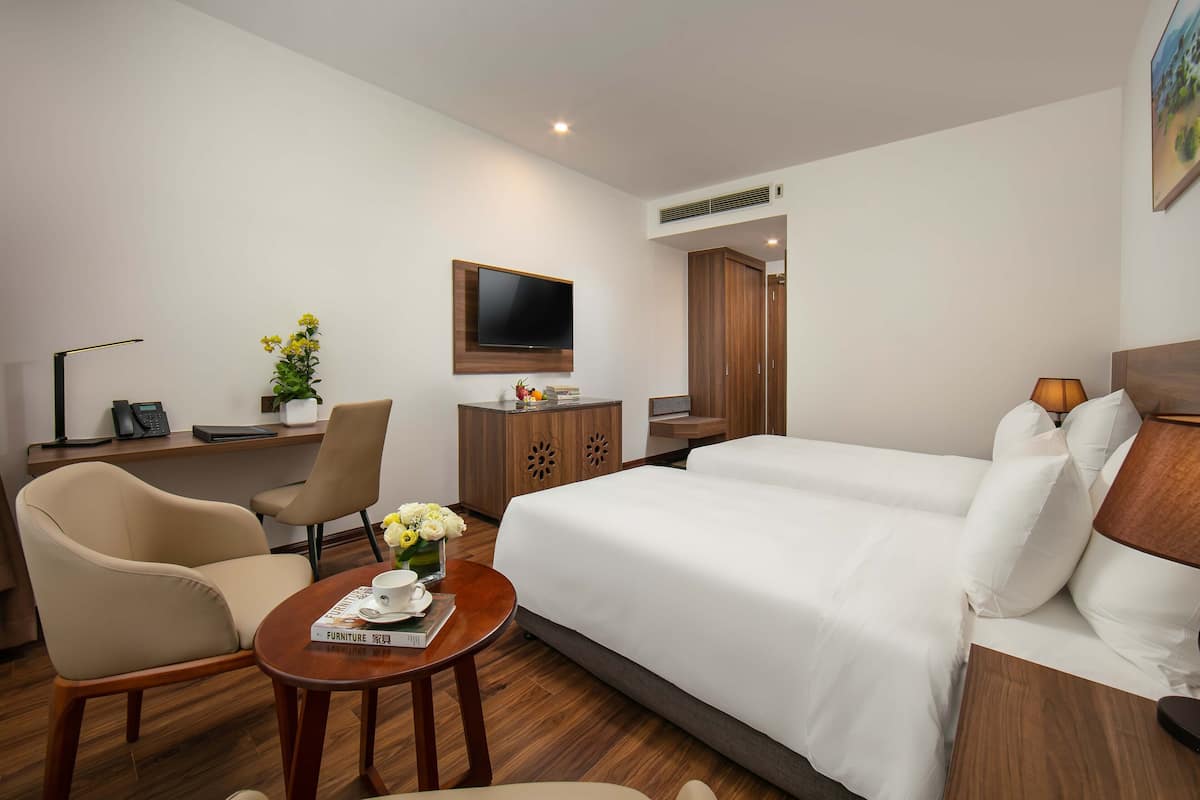 Ein Hotelzimmer mit einem Bett, zwei Stühlen, einem Schreibtisch, einem Fernseher und einem kleinen Tisch mit einer Blumenvase.