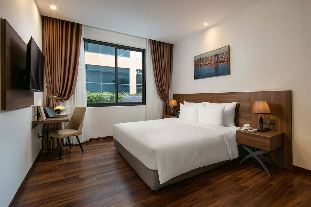 Ein Hotelzimmer mit einem großen Bett, einem Schreibtisch mit Stuhl, einem Fernseher und einem Stadtbild.