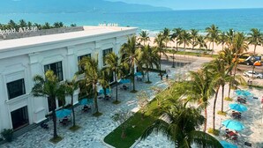 Un patio de hotel con palmeras, mobiliario exterior y vistas al océano.