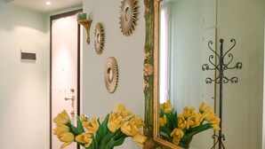 A hallway with a mirror, decorative wall pieces, and a vase of yellow flowers. - The Green House in Trastevere (Roma)