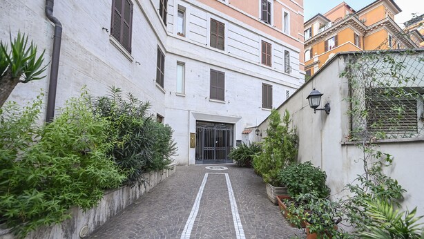 A narrow cobblestone alleyway flanked by buildings with white and orange facades, leading to a gated entrance. - The Green House in Trastevere (Roma)