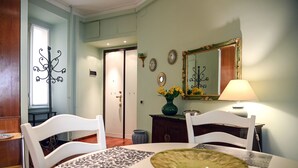 A dining area with a round table, white chairs, a vase with yellow flowers, and a mirror on the wall. - The Green House in Trastevere (Roma)