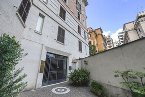 A narrow alleyway with a gated entrance, a tiled pavement, and a wall with a small plant.