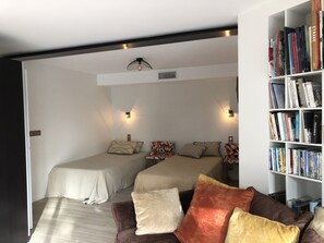 A compact room with two beds, a bookshelf, and a sofa with cushions.