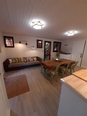 A compact living space with a sofa, dining table, and chairs, a kitchenette, and a door leading to a balcony.