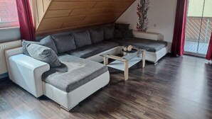 Una sala de estar moderna con techo inclinado, un sofá modular, una mesa de centro de vidrio y vistas a un balcón.