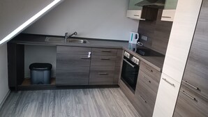 Una cocina compacta con horno integrado, un lavamanos y un hervidor sobre la encimera.