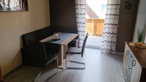 Una habitación compacta con una mesa de madera, dos sillas, un sofá negro y un mueble pequeño.
