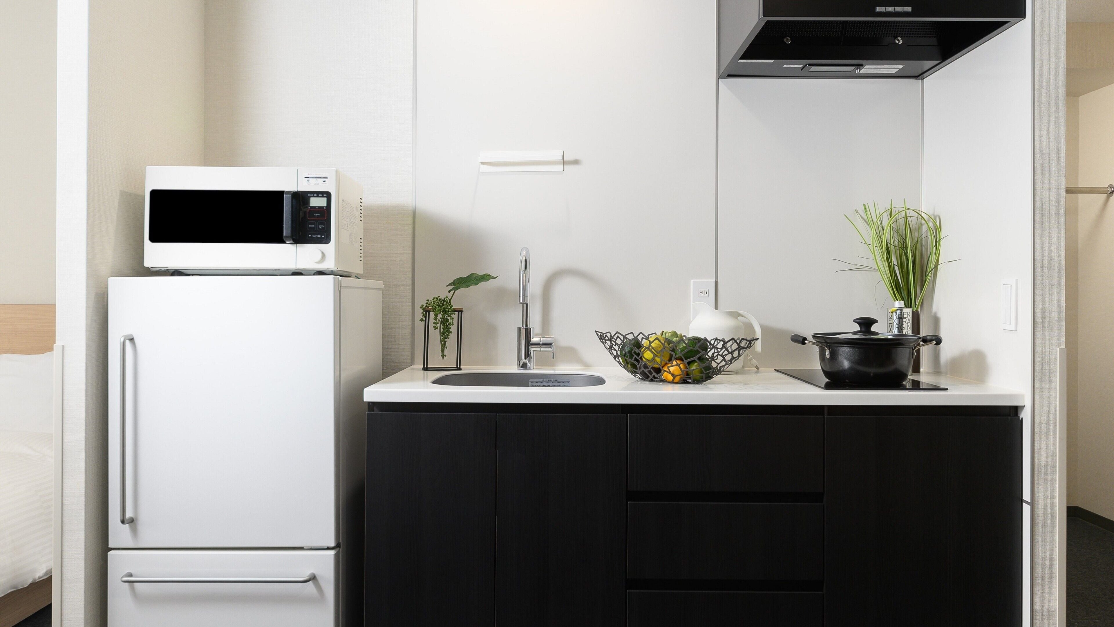A compact kitchen with a white refrigerator, a microwave, a sink with a modern faucet, a black pot on the counter, and a potted plant.