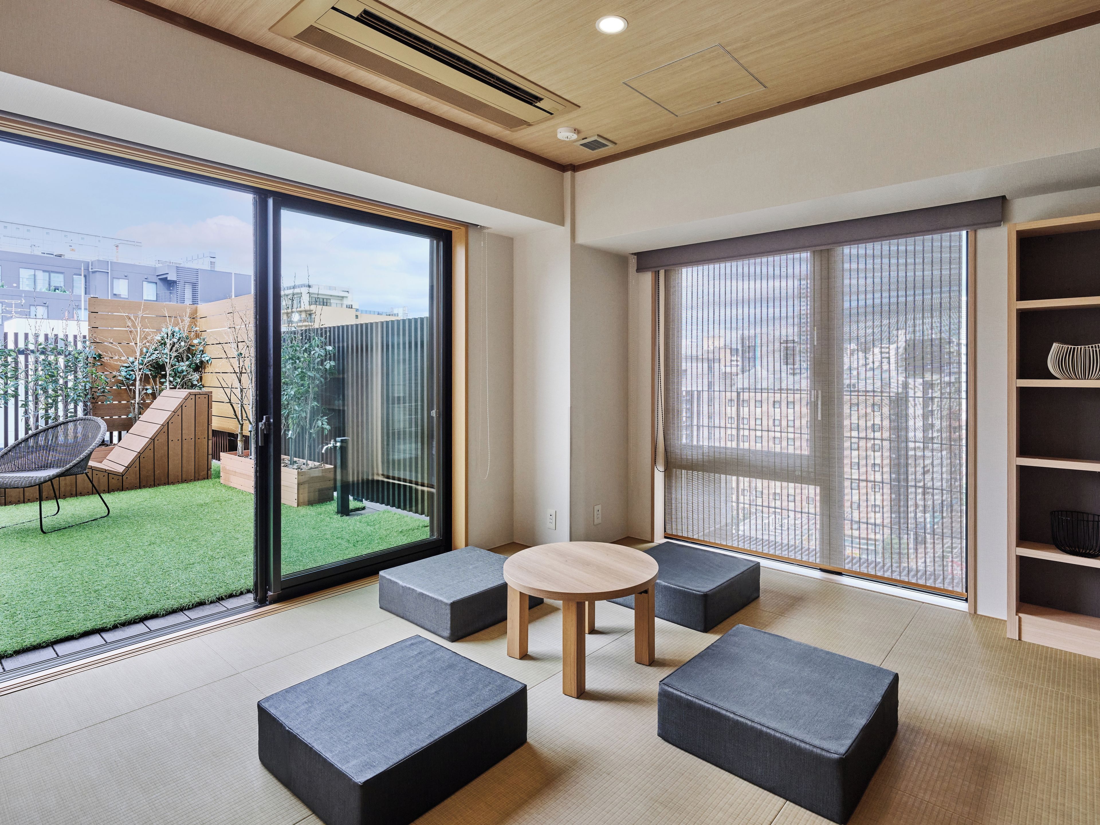 Ein modernes Interieur mit einer Schiebeglastür, die auf einen Balkon führt, einem runden Holztisch und grauen Sitzgelegenheiten.