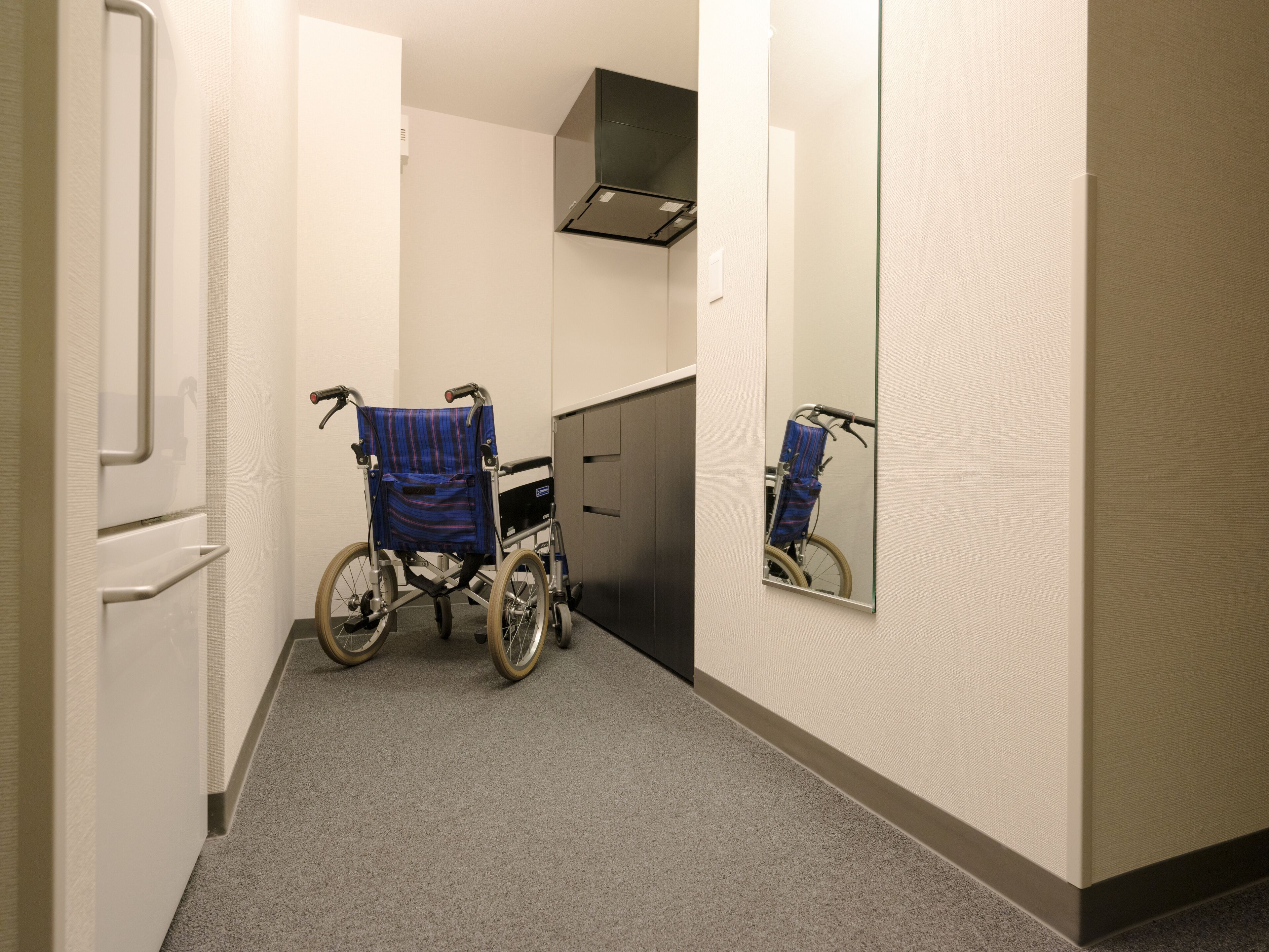 A wheelchair in a hallway with a mirror reflecting the wheelchair and a bicycle.