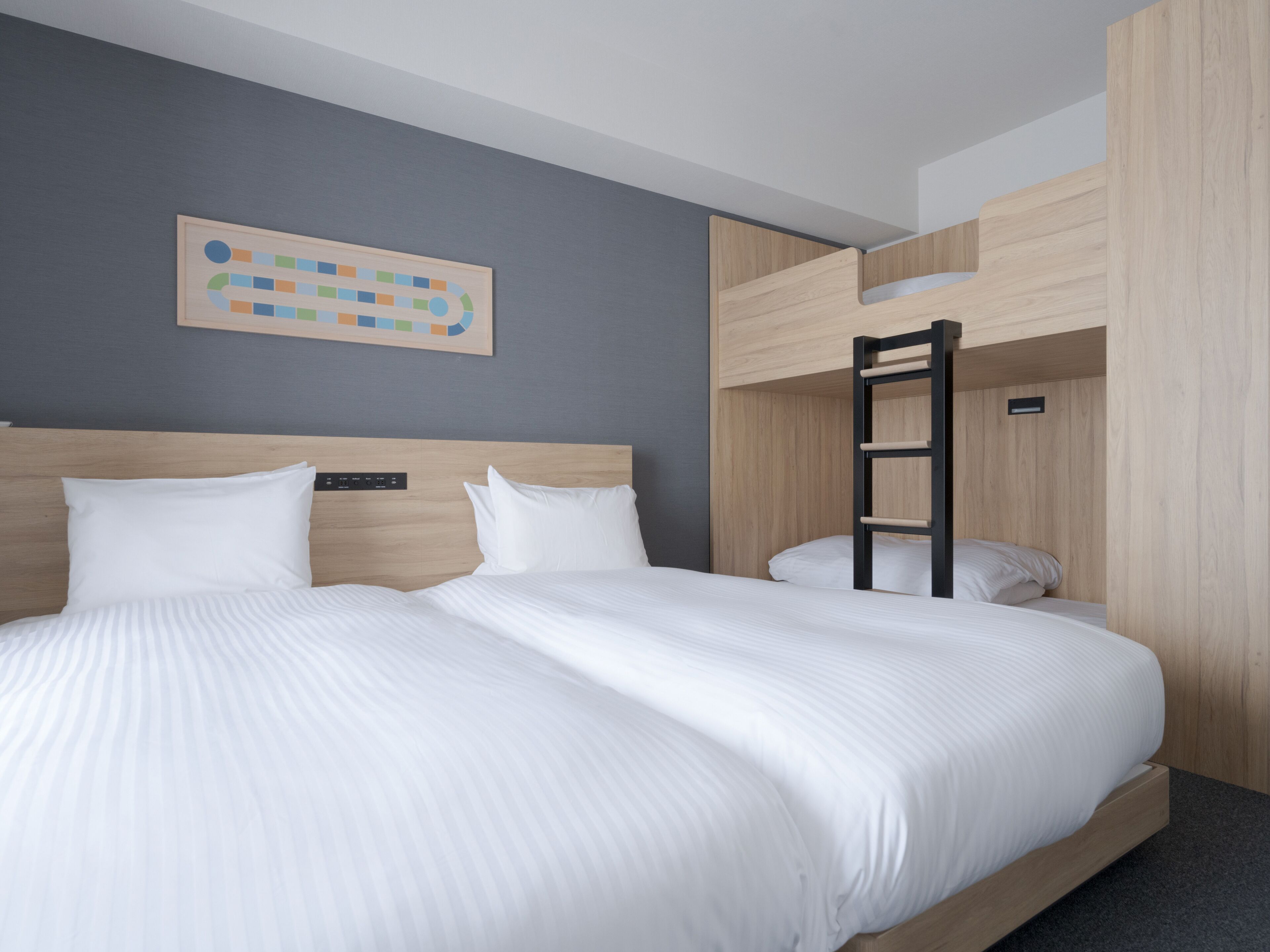 A hotel room with a large bed, a headboard with controls, a wooden ladder, and a wall-mounted artwork.