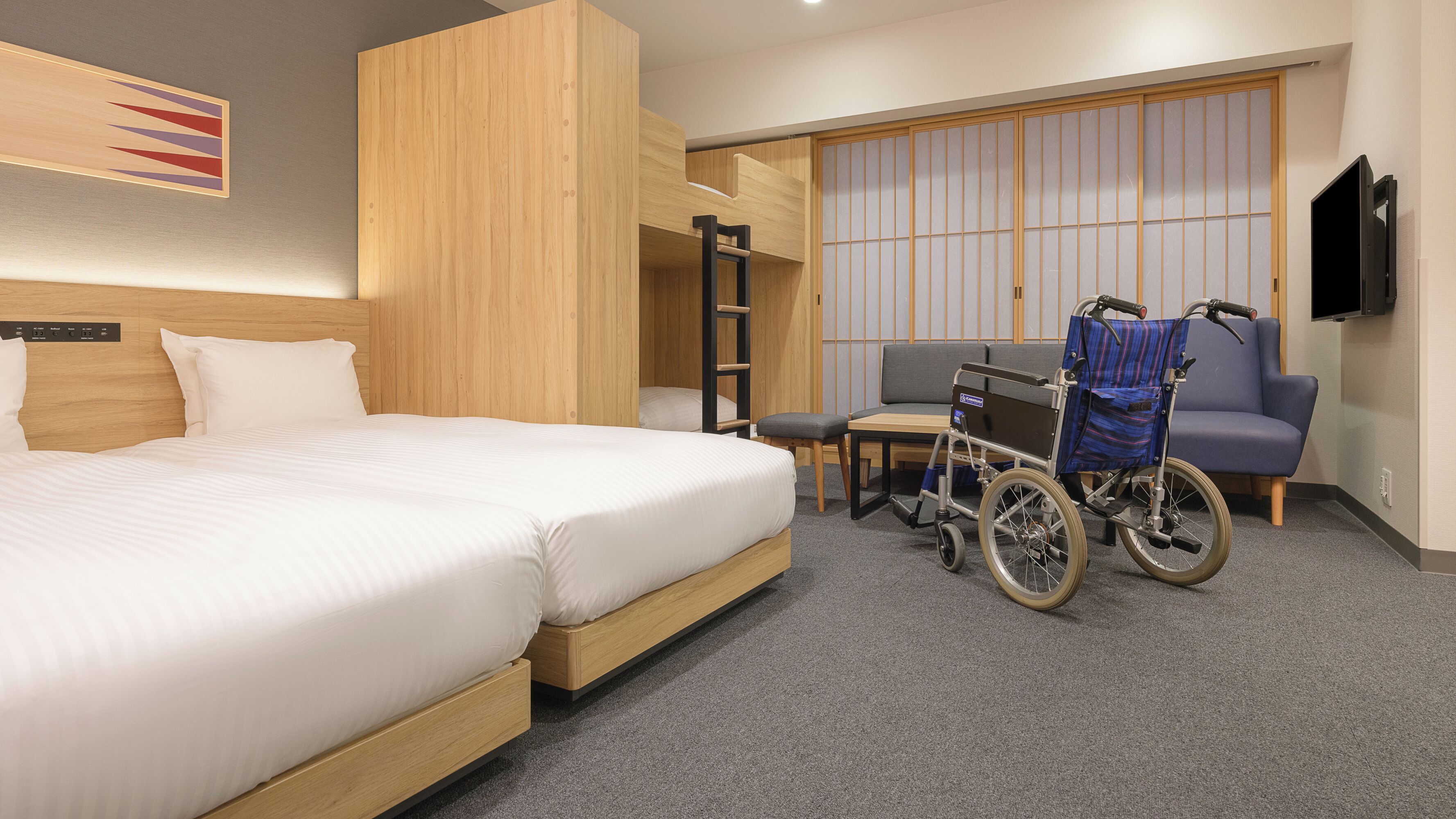 A hotel room with a large bed, a wheelchair, a small table, and a sofa.