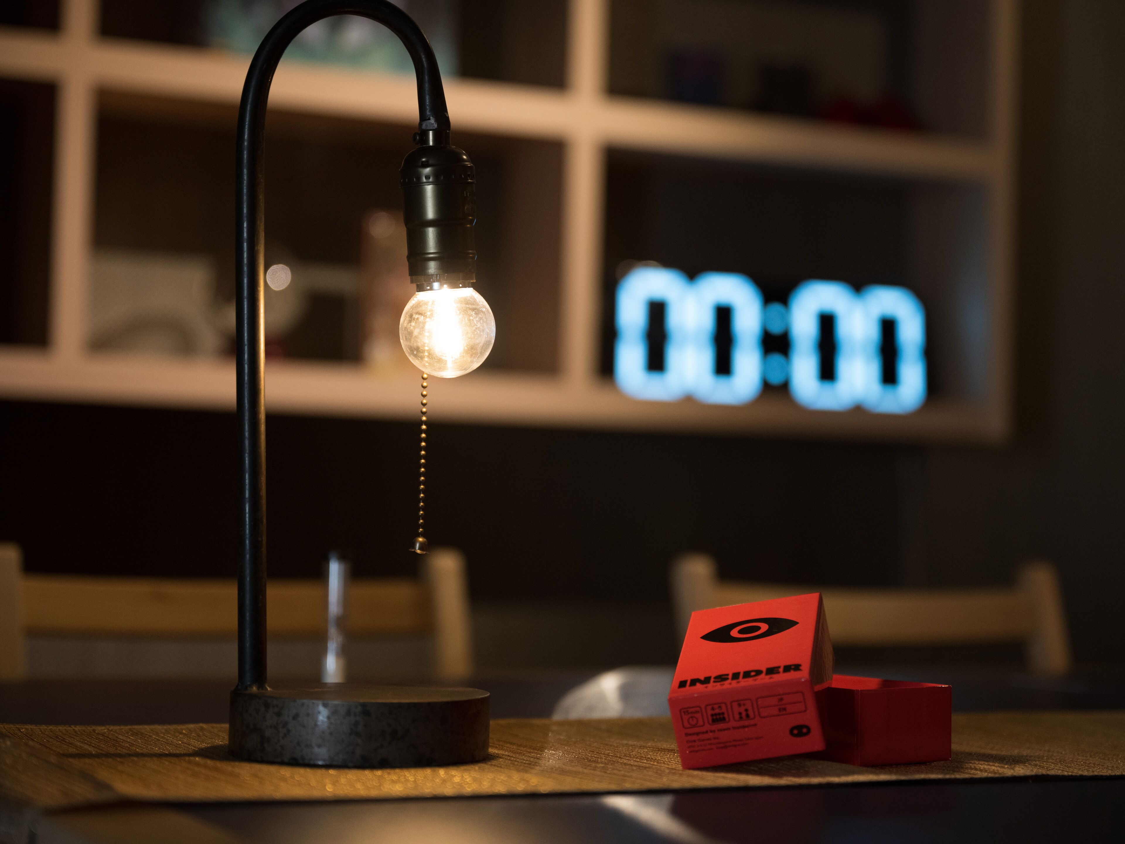 Una lámpara de escritorio con un temporizador visible ajustado a 00:00, una caja roja etiquetada “INSIDER” y una superficie de madera.