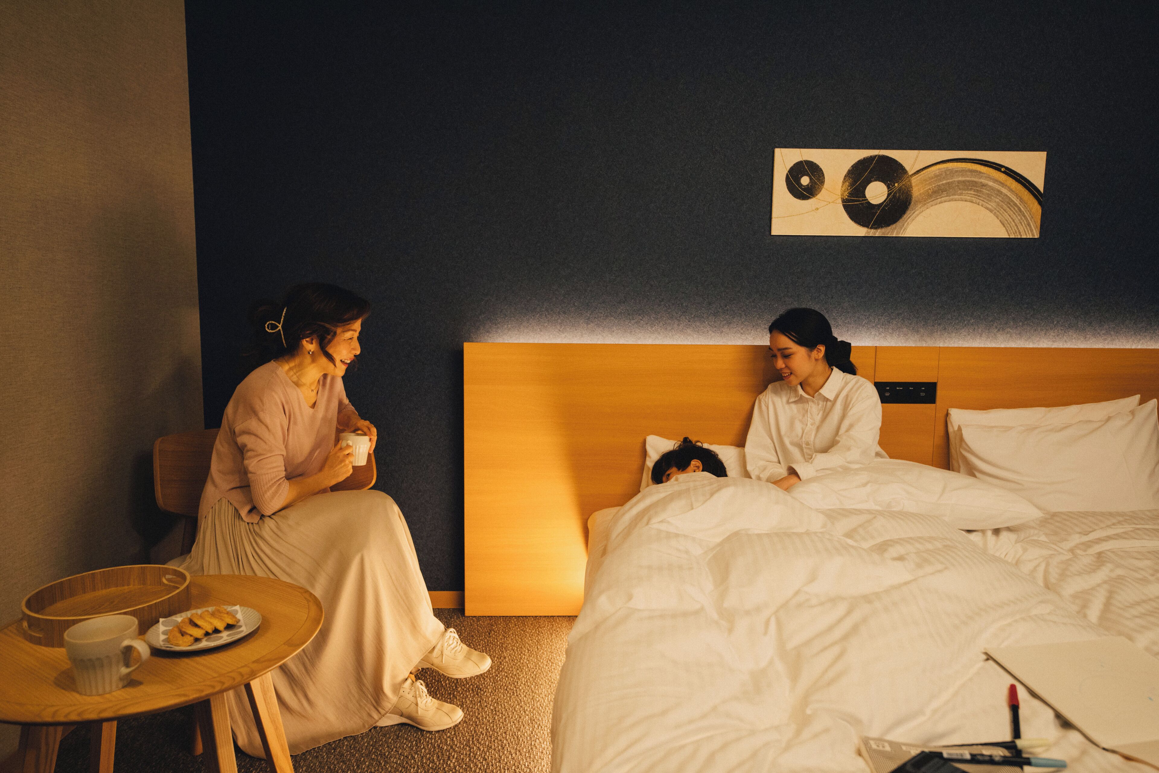 A hotel room with a bed, a bedside table with a cup and plate, and a wall art piece.