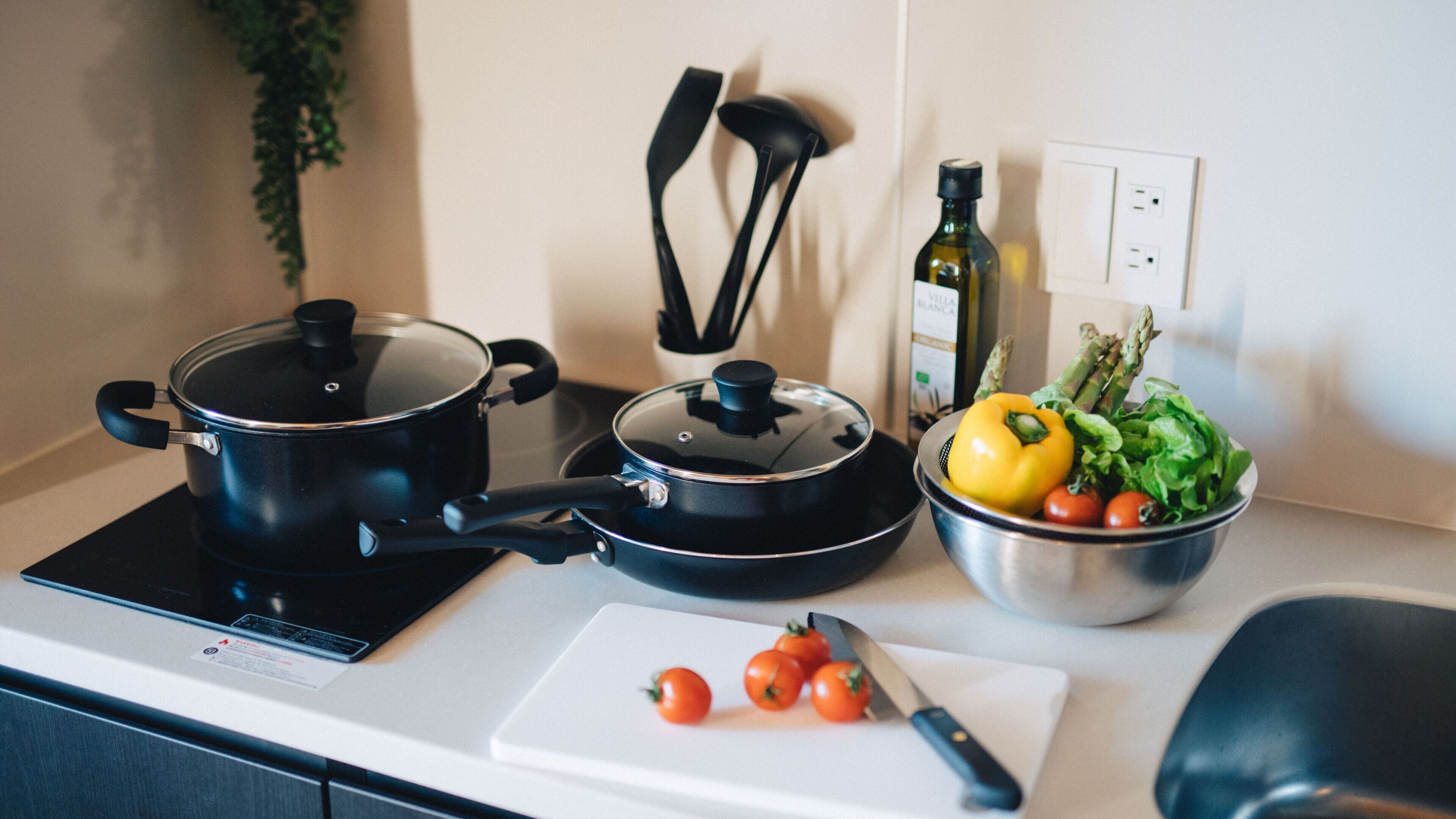 A kitchen with two electric stoves, a pot on one, and a bowl of vegetables on the counter.