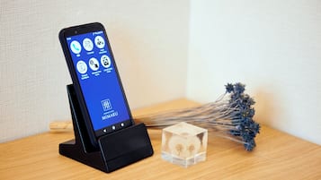 Un smartphone placé sur une station de recharge affiche une application d’hôtel proposant diverses fonctionnalités, telles que des options de langue, des informations sur l’hôtel et des détails sur l’état des chambres.