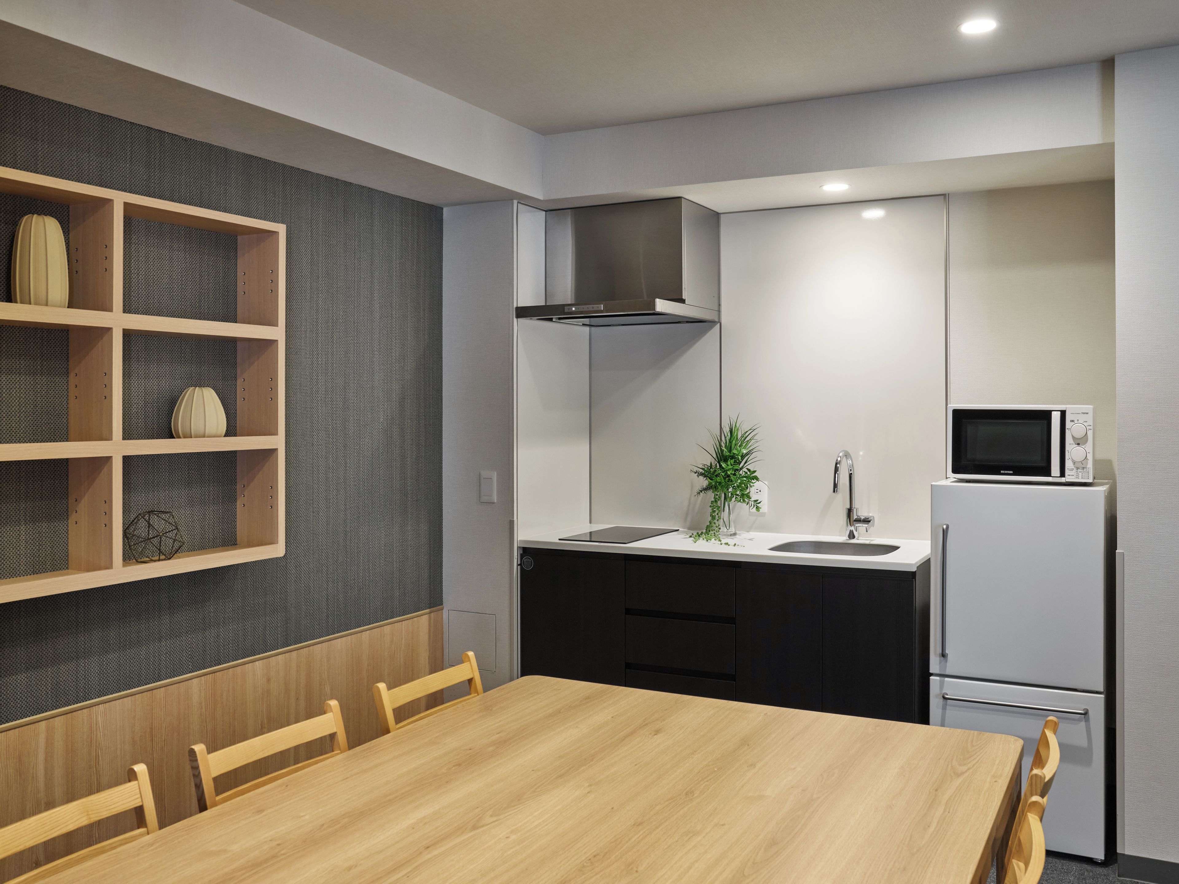 A modern kitchen with a wooden dining table, built-in shelves, a microwave, and a refrigerator.