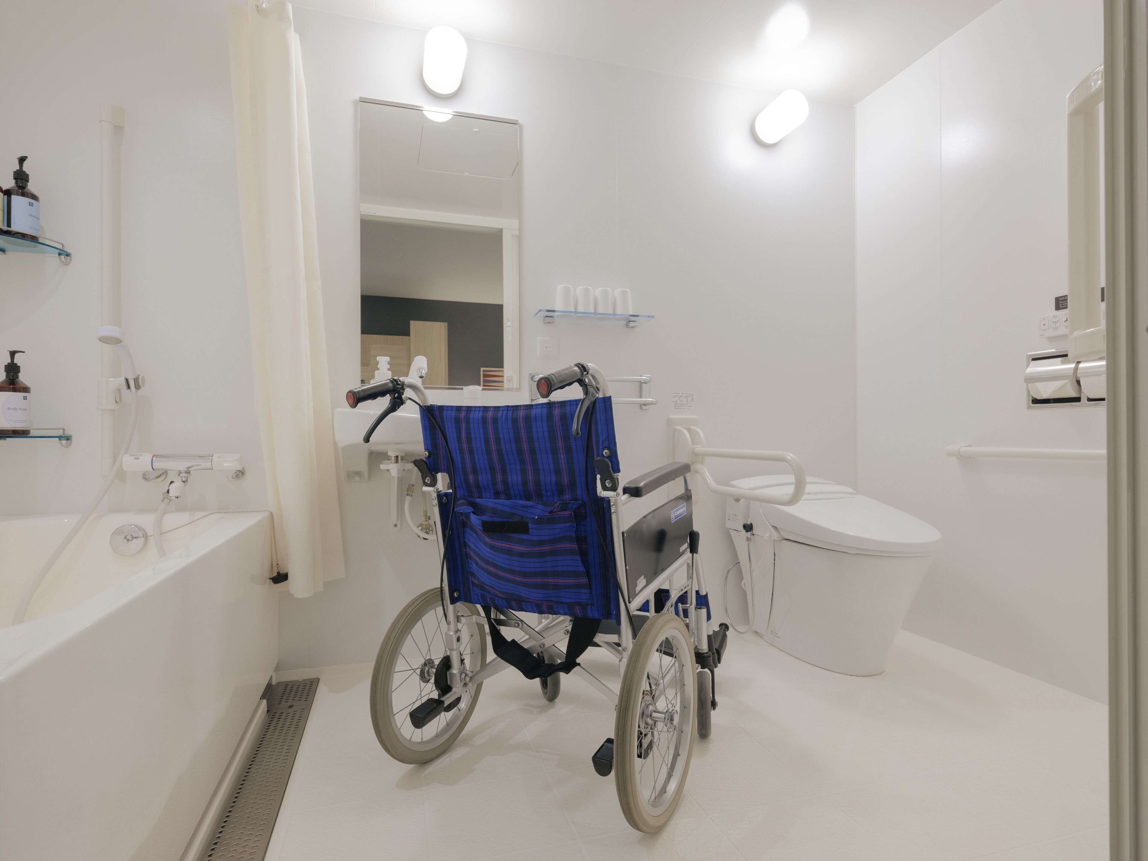 Une salle de bain accessible aux personnes en fauteuil roulant, équipée de toilettes, d’un lavabo et d’un miroir.