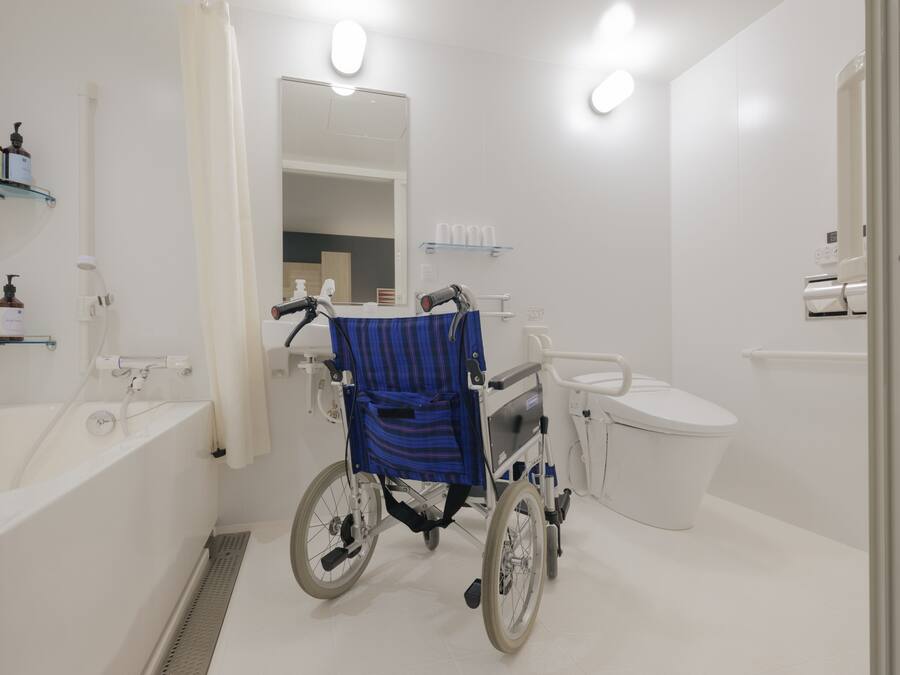 Une salle de bain accessible aux personnes en fauteuil roulant, équipée de toilettes, d’un lavabo et d’un miroir.