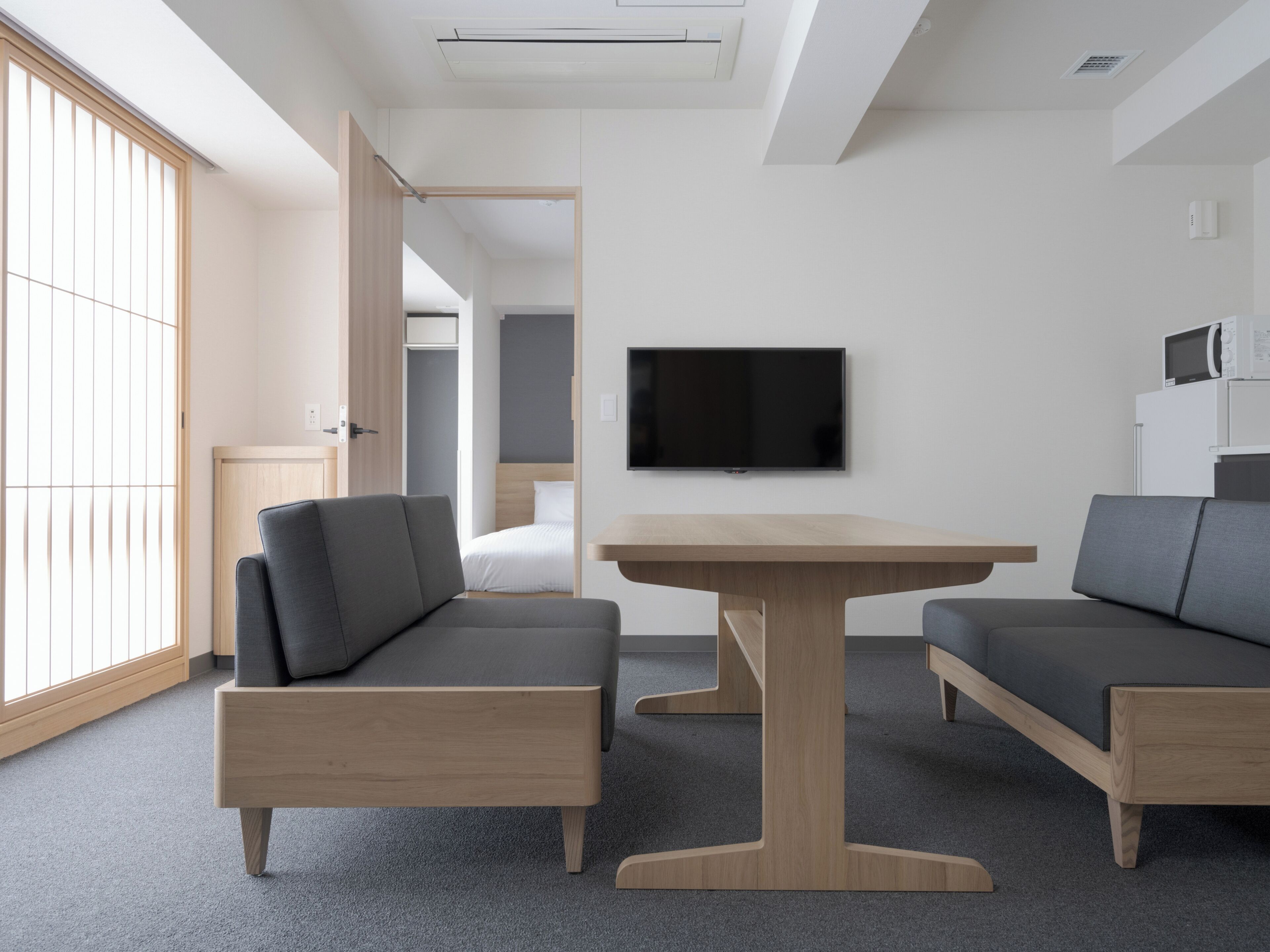 A modern, minimalist room with a sofa set, a wooden table, and a flat-screen TV mounted on the wall.