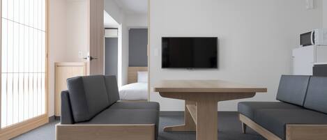 A modern, minimalist room with a sofa set, a wooden table, and a flat-screen TV mounted on the wall.