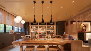 A modern interior with a wooden dining table, chairs, pendant lights, and a bookshelf filled with books and games. - MIMARU Osaka Namba Station (Osaka)