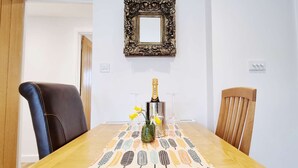 A dining table with a decorative tablecloth, a bottle of champagne, and two glasses. - Beautifully  Presented One Bedroom Romantic Home & Private Hot Tub. (WEST LOOE)