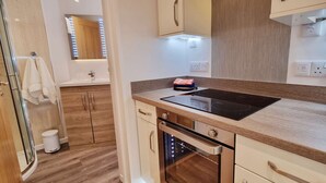 A modern kitchen with a built-in induction cooktop, a kettle, and wooden cabinets. - Beautifully  Presented One Bedroom Romantic Home & Private Hot Tub. (WEST LOOE)