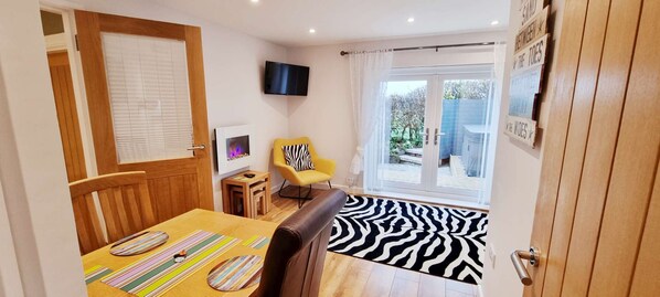 Une pièce chaleureuse avec une table à manger en bois, un tapis à motifs zébrés, un fauteuil jaune et un téléviseur à écran plat fixé au mur.