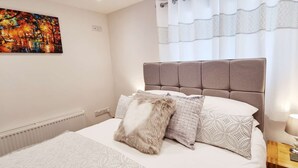 A bedroom with a bed, a headboard, a nightstand with a lamp, and a painting on the wall. - Beautifully  Presented One Bedroom Romantic Home & Private Hot Tub. (WEST LOOE)
