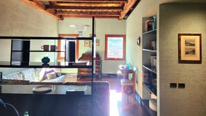 Un intérieur rustique avec des poutres apparentes, une cheminée, un canapé, une table à manger et une bibliothèque.