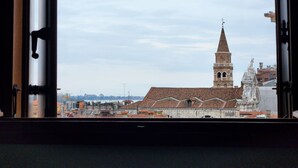 Une vue sur une église dotée d’un haut clocher et d’un toit recouvert de tuiles, prise à travers une fenêtre.