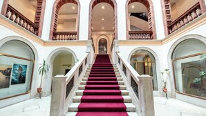 Un magnifique escalier, recouvert d’un tapis rouge, mène à l’étage supérieur et est bordé de fenêtres en arc et de balustrades richement décorées.