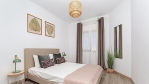 Un dormitorio con cama, mesita de noche, lámpara, espejo y ventana con cortinas.