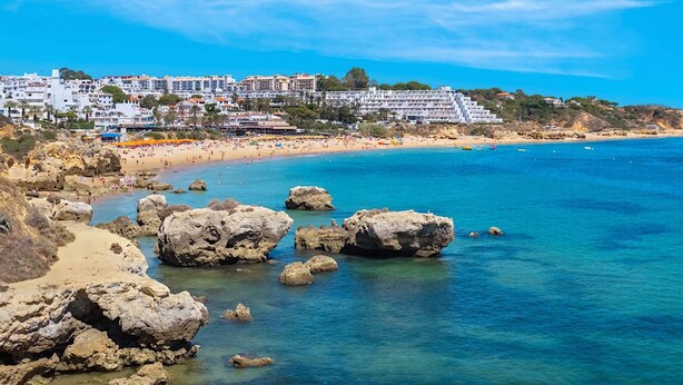 Un pueblo costero con playa, costa rocosa y edificios al fondo.
